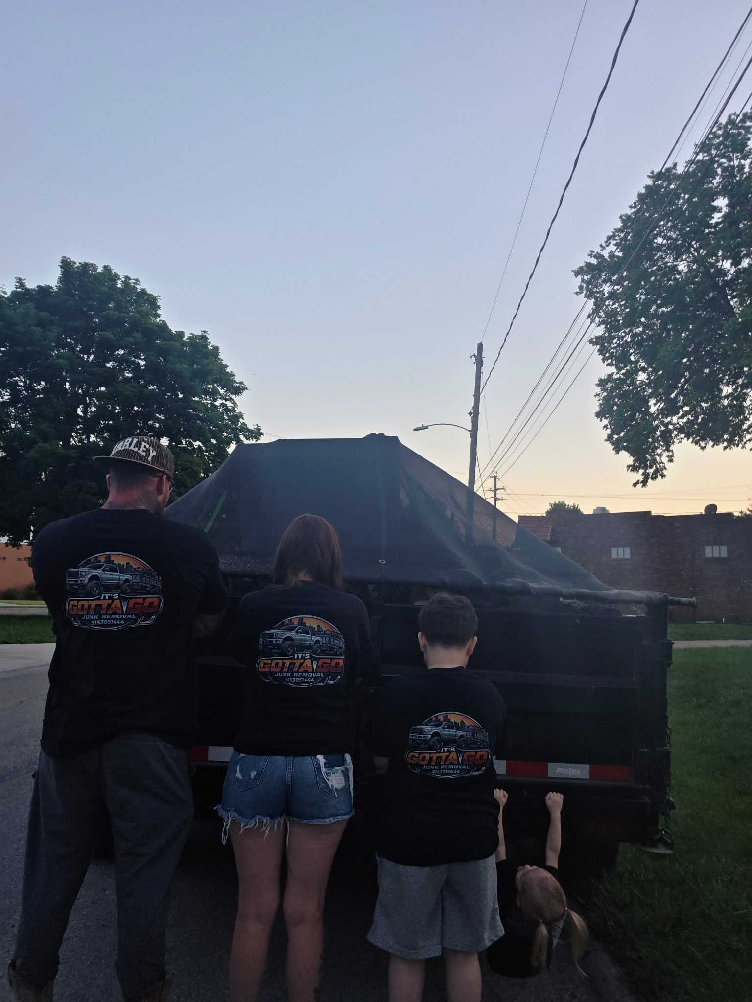 Its Gotta Go crew in branded shirts in front of loaded trailer at dusk