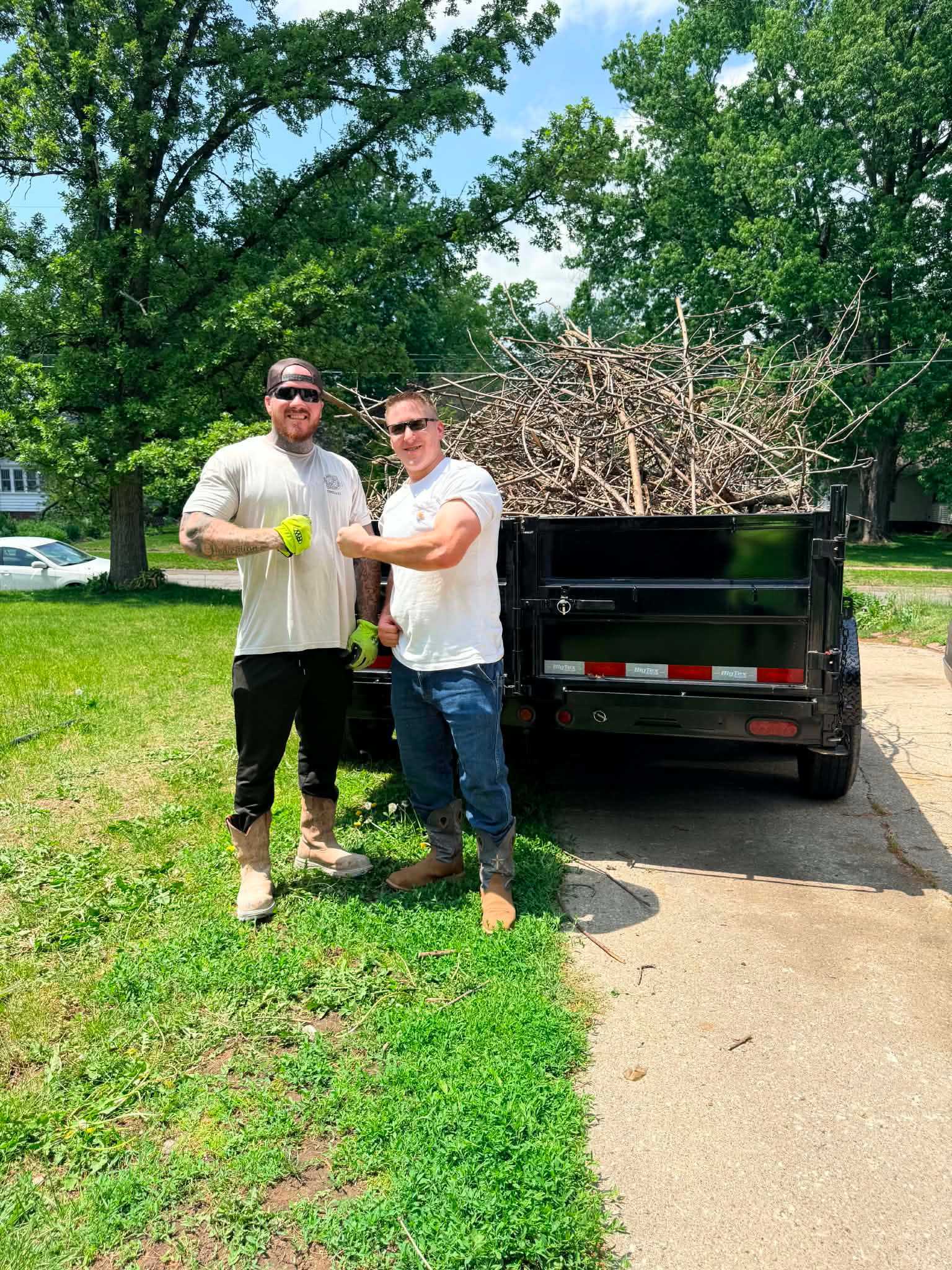 Two crew members giving thumbs up in front of brush trailer